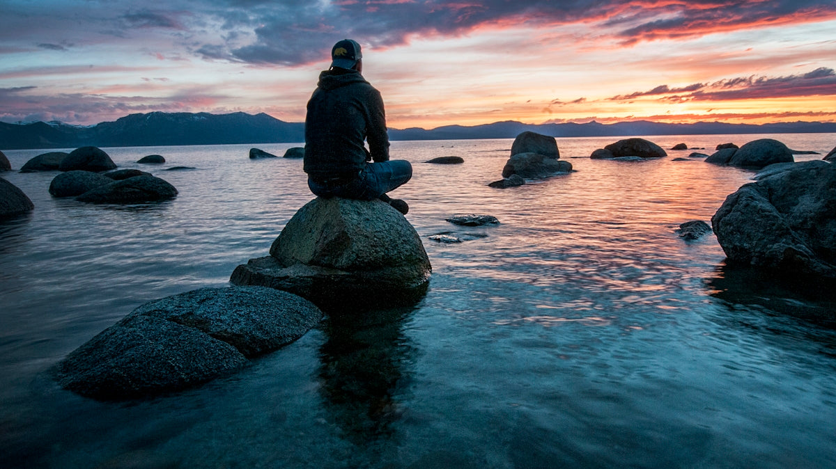 man sitting on rock surrounded by water