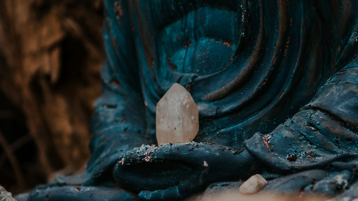Buddha statue holds crystal; weathered, peaceful, spiritual