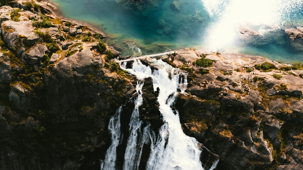 A powerful waterfall cascades over rocky cliffs into blue water.