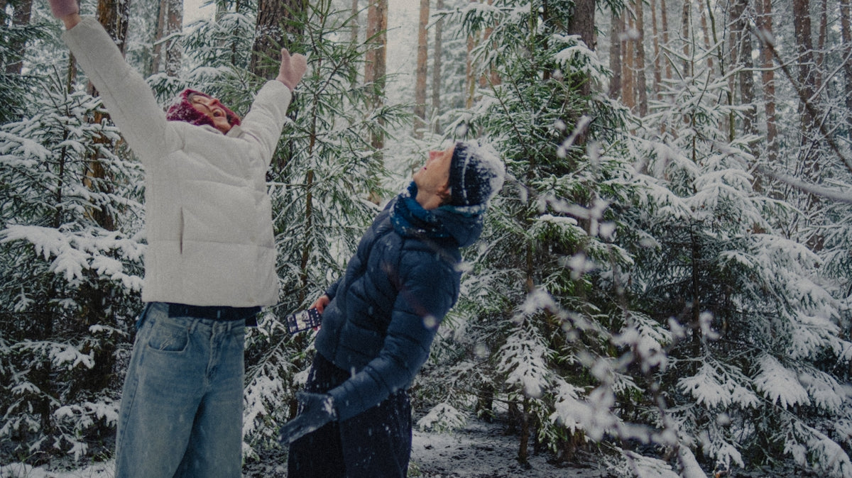 Two people enjoying snowfall in a winter forest.