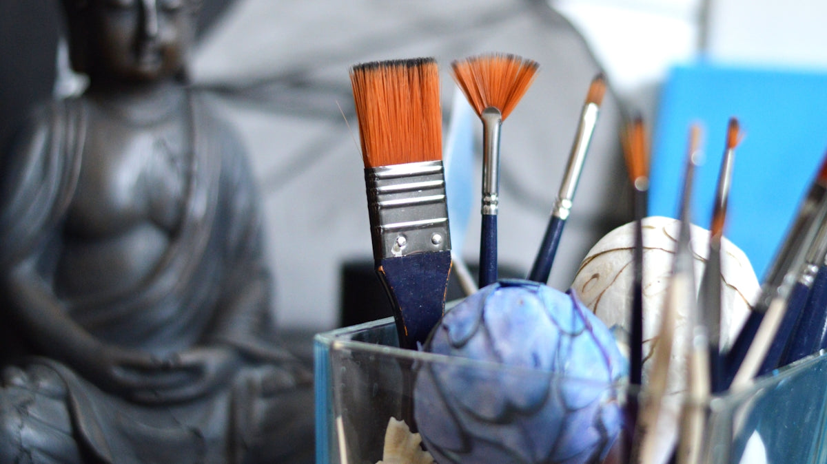 Art brushes in a glass with buddha statue background.