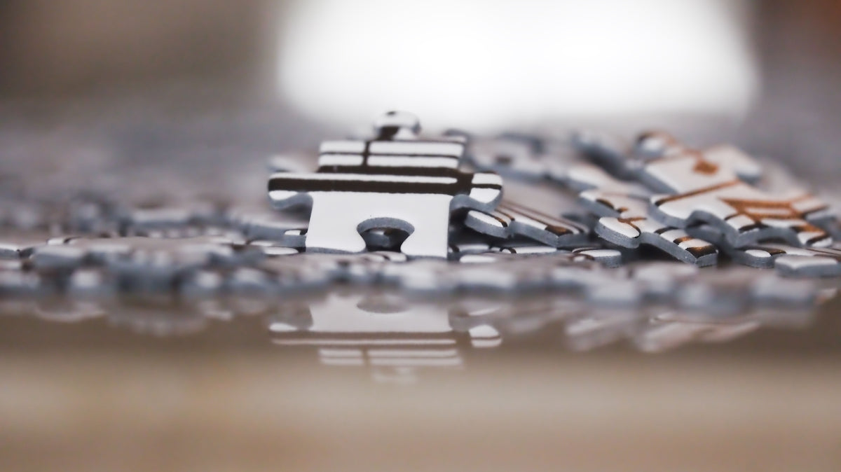 Scattered puzzle pieces on a reflective surface, one standing upright