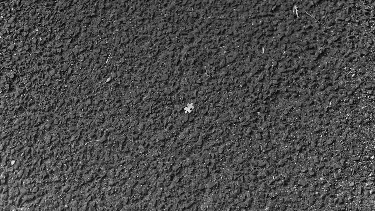 A single puzzle piece on a dark textured asphalt surface