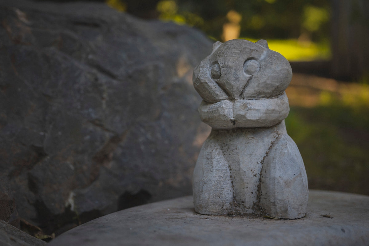 Wooden owl carving sits on a rock outdoors.