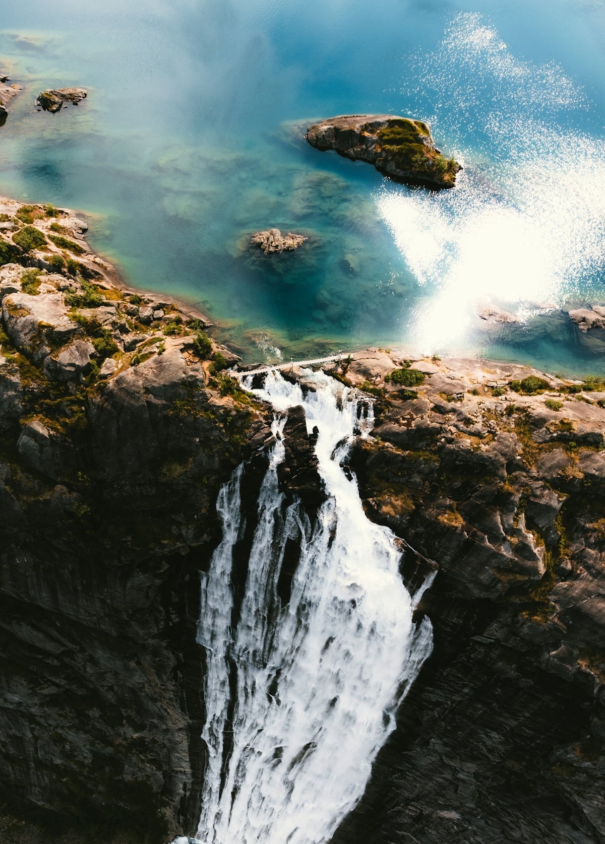 A powerful waterfall cascades over rocky cliffs into blue water.