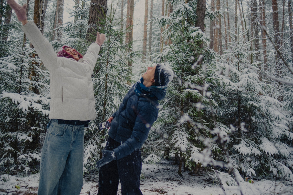 Two people enjoying snowfall in a winter forest.
