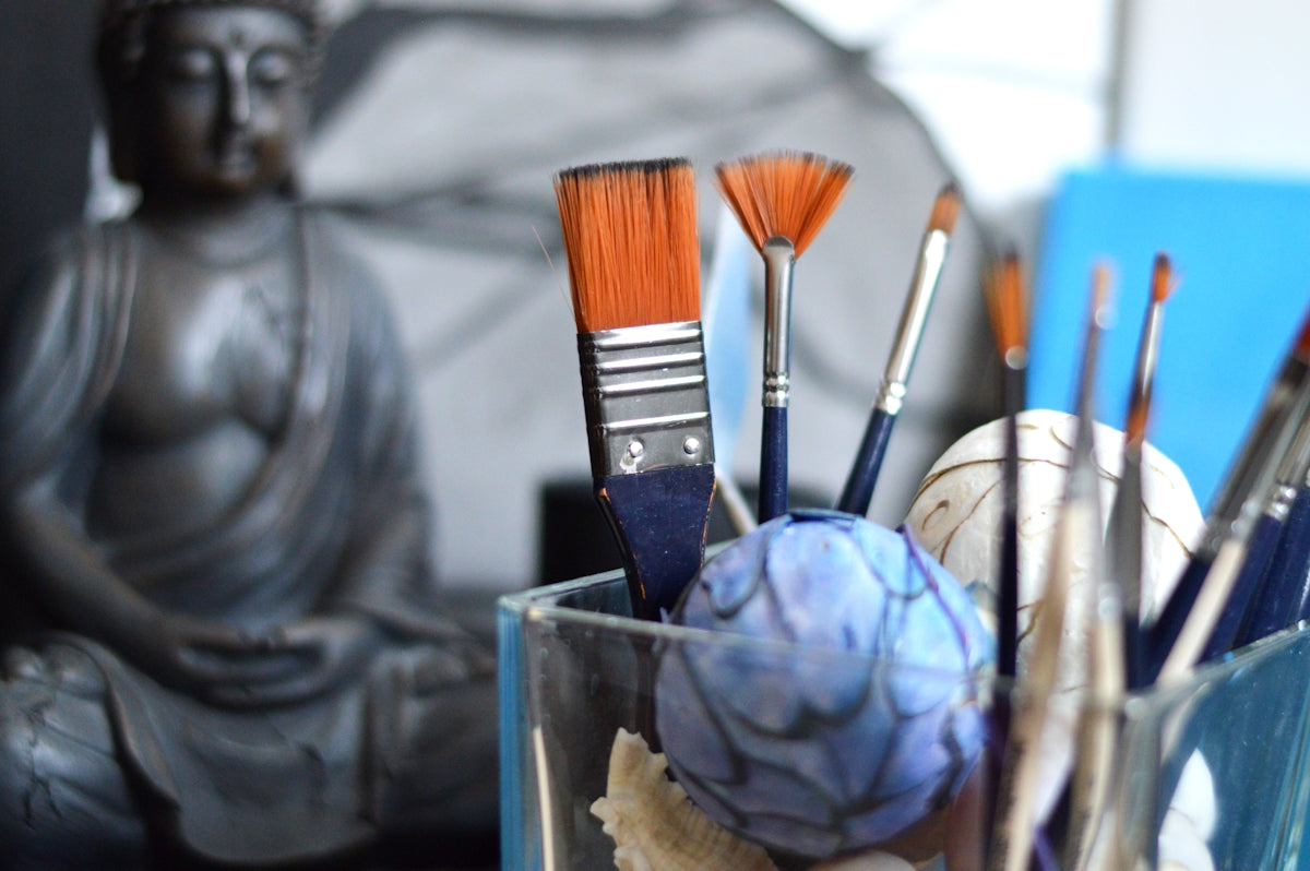 Art brushes in a glass with buddha statue background.