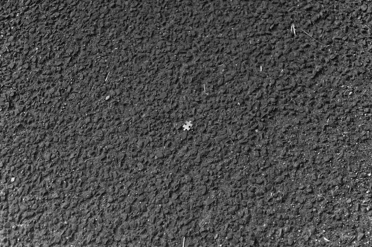 A single puzzle piece on a dark textured asphalt surface
